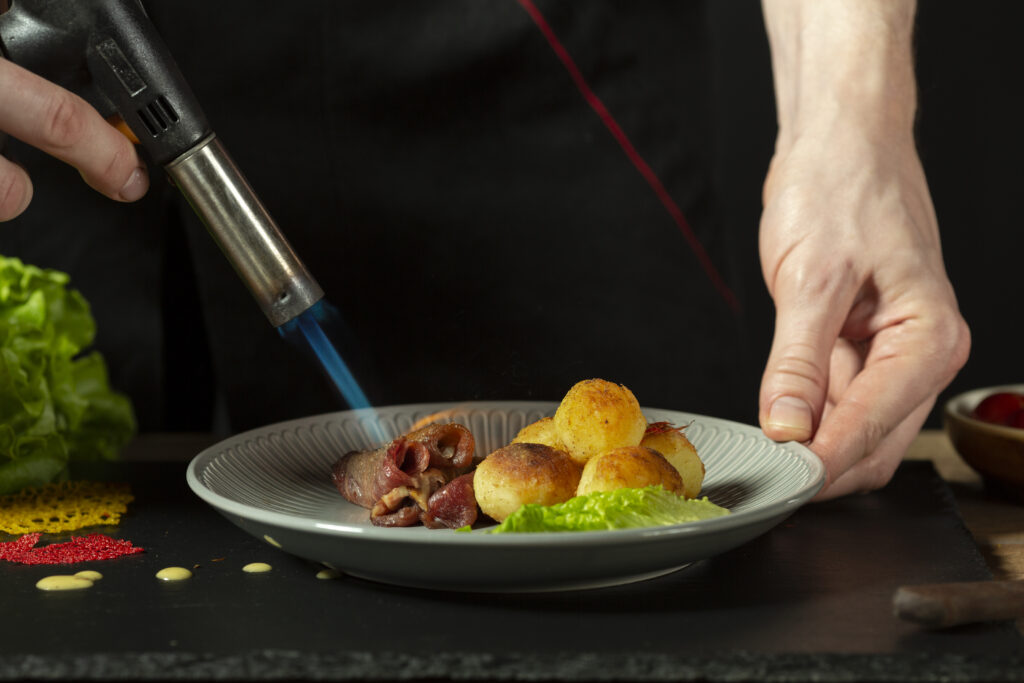 Culinary torch caramelizing sugar on crème brûlée, demonstrating professional kitchen torching techniques for home cooking.
