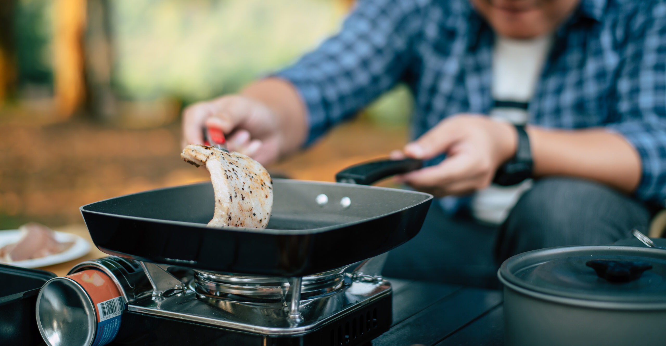 Traveler cooking pork steak in a skillet at a campsite, showcasing outdoor travel cooking and camping lifestyle.